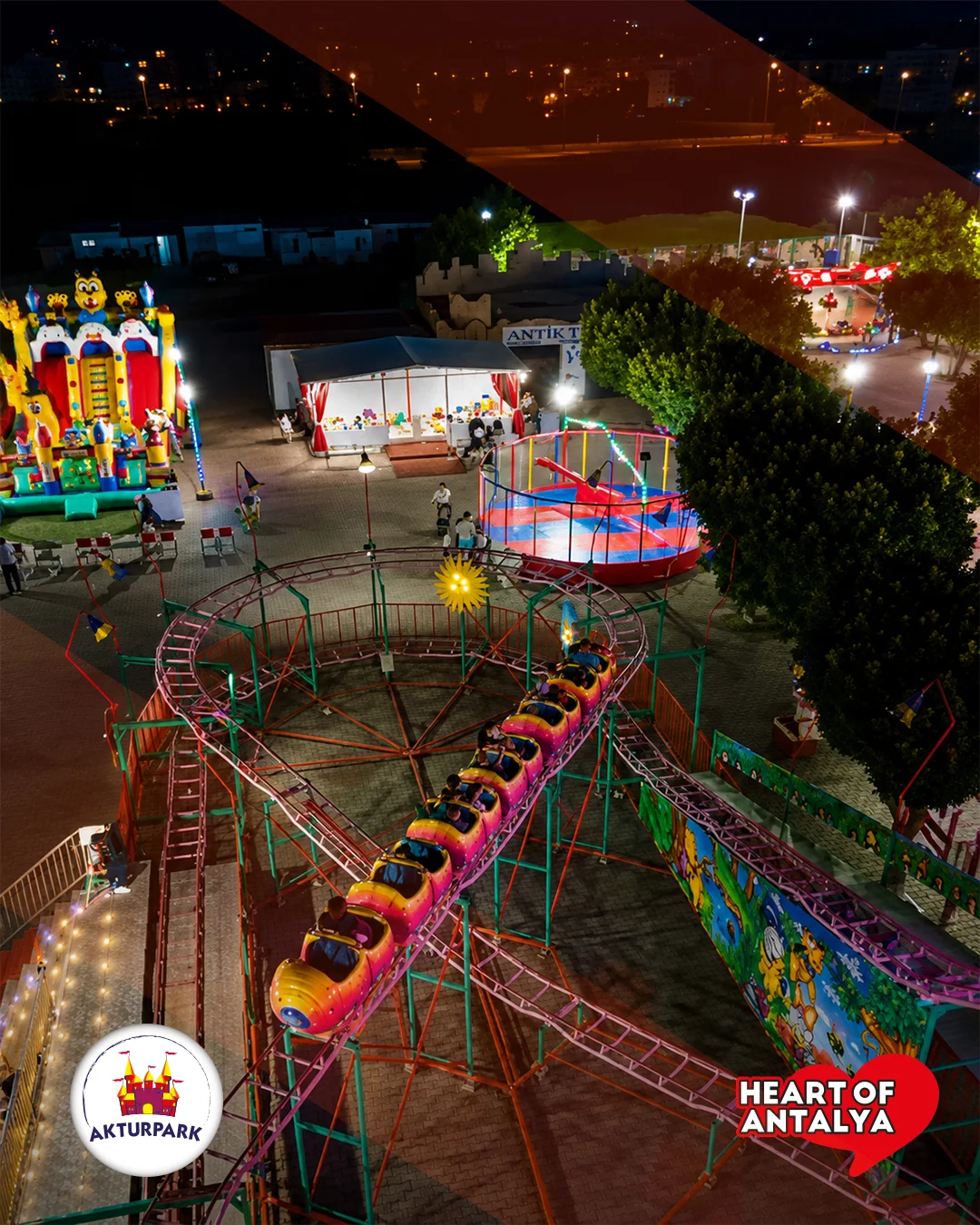 Gece yukarıdan görülen kıvrımlı mini roller coaster ve ışıklı park.
