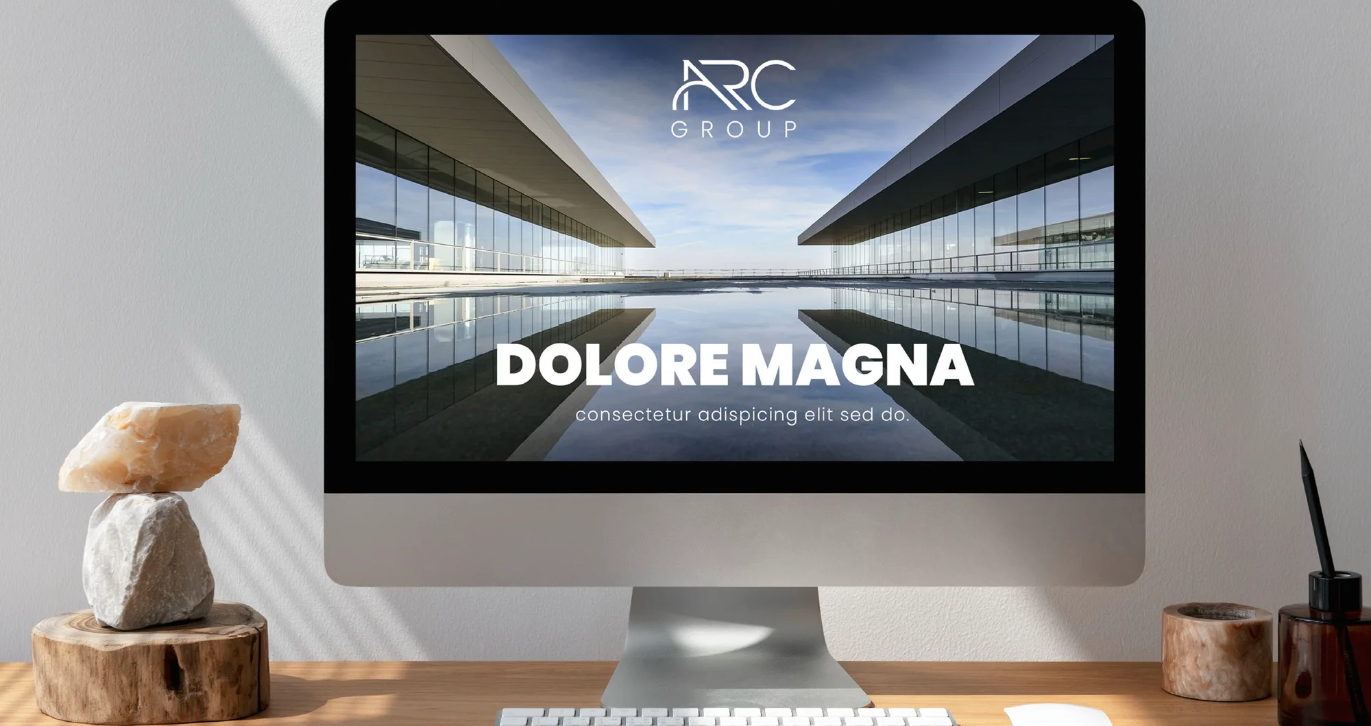 A web banner template on a monitor on a wooden desk: logo and headline area over a photo of modern architecture.