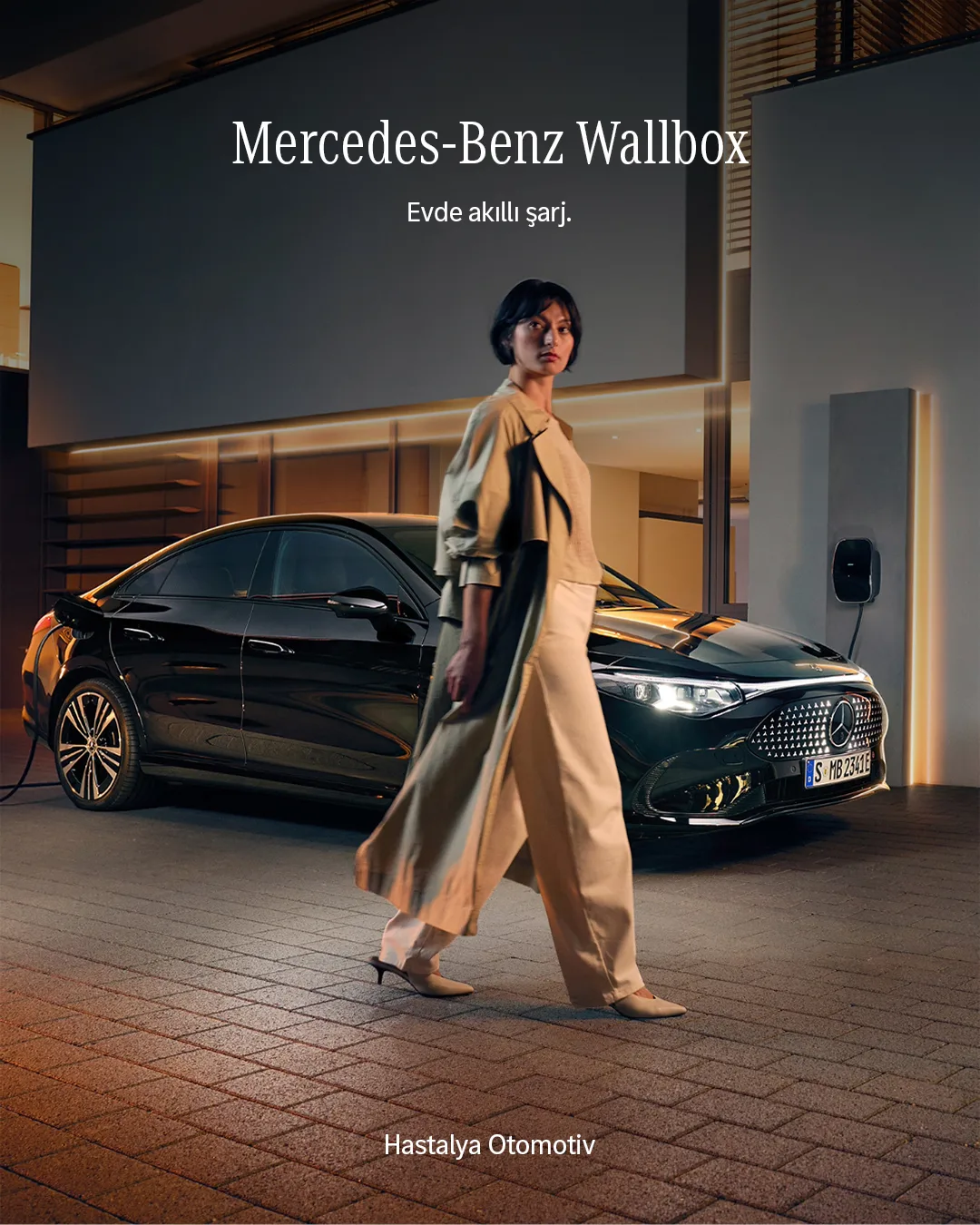 Akşam ışığında modern evin önünde yürüyen trençkotlu kadın ve şarjdaki siyah Mercedes; "Mercedes-Benz Wallbox" başlığı.