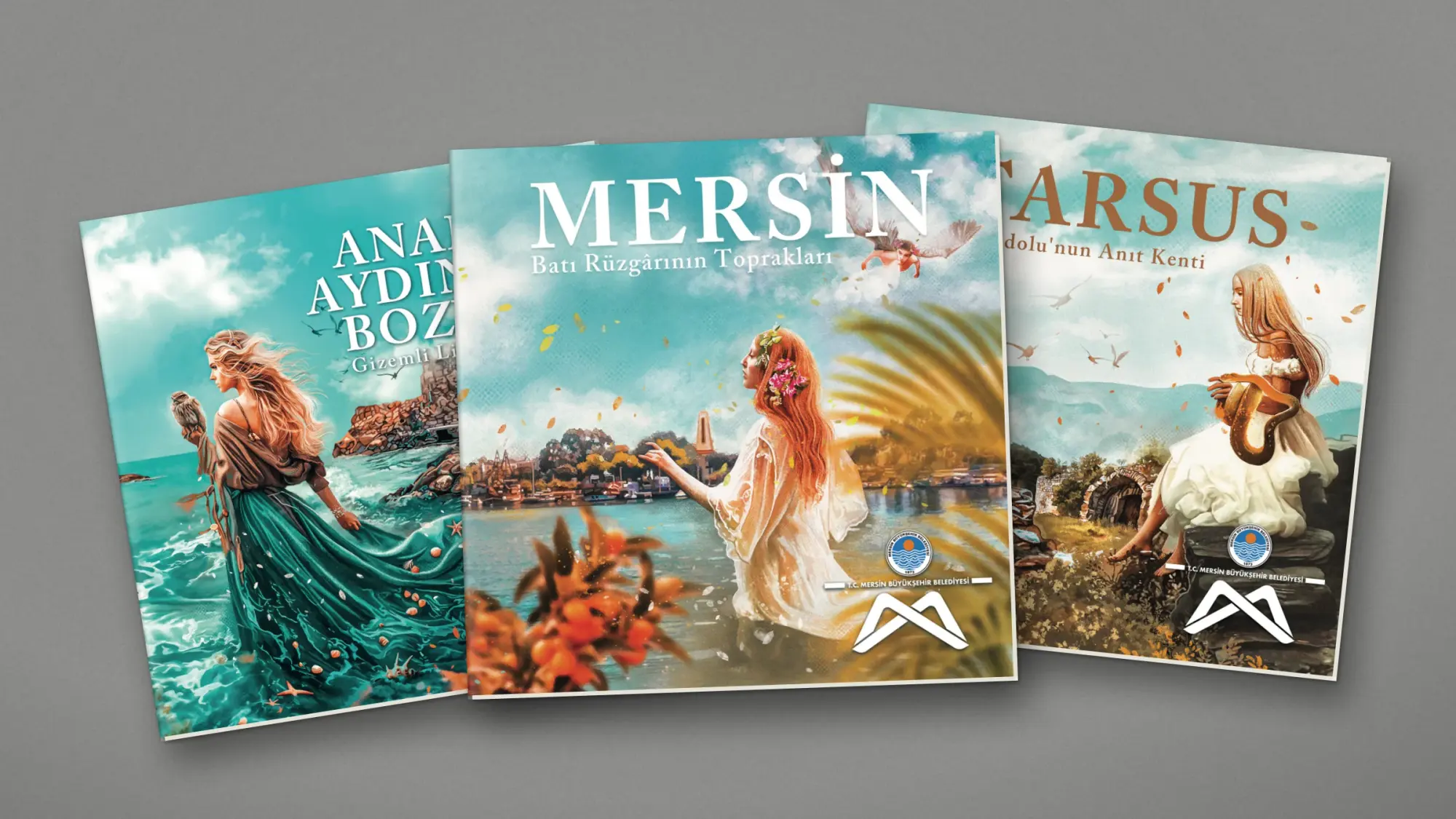 Gri keçe üzerinde yelpaze gibi açılmış üç kitapçık: ortada "MERSİN — Batı Rüzgârının Toprakları", solda Anamur Aydıncık Bozyazı, sağda "TARSUS — Anadolu’nun Anıt Kenti"; kapaklarda illüstratif kadın figürleri.