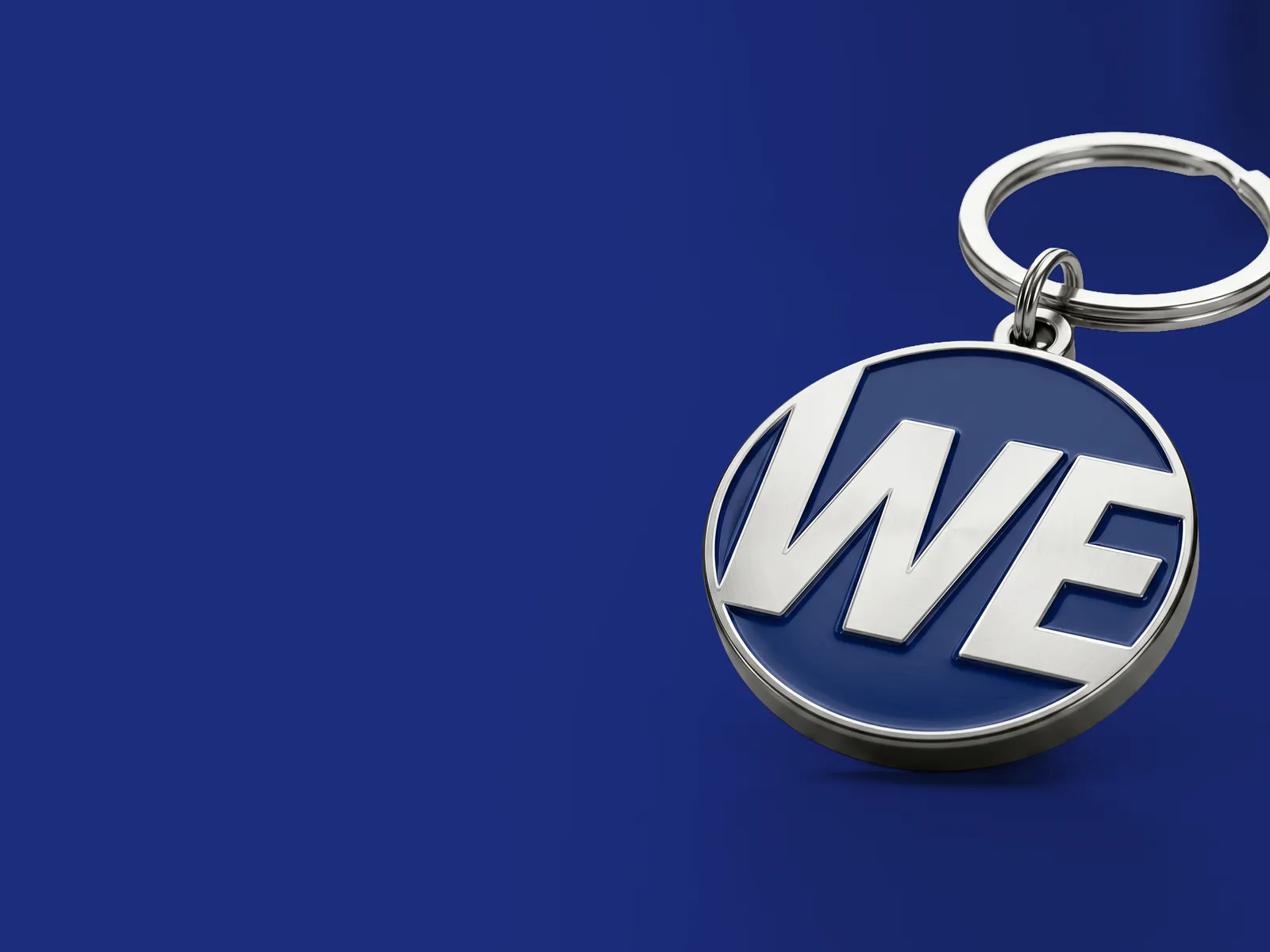 Navy car key ring with chrome WE letters, on blue.